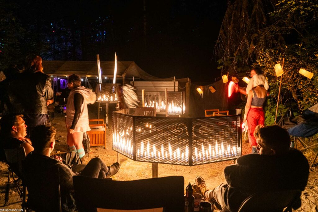 People relaxing around a metal flame effect sculpture designed to look like a dragon. The design consists of walls of fire behind a decorative lasercut frame. 